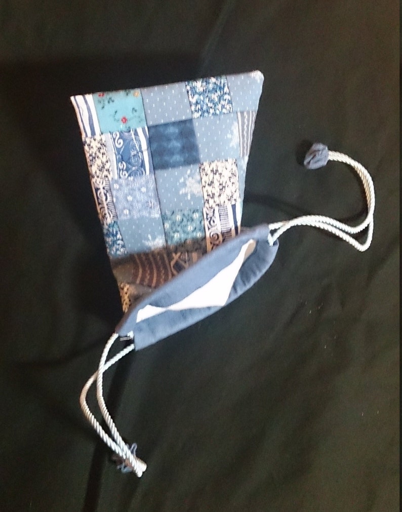 May include: A blue patchwork drawstring bag with a white lining. The bag is made of various blue and white fabrics and has a white drawstring.
