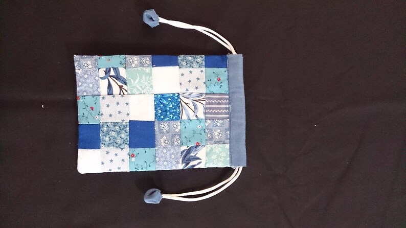 May include: A small blue and white patchwork drawstring bag with a white cord.
