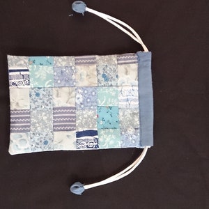 May include: A small blue drawstring bag with a patchwork design of various shades of blue and white fabric.