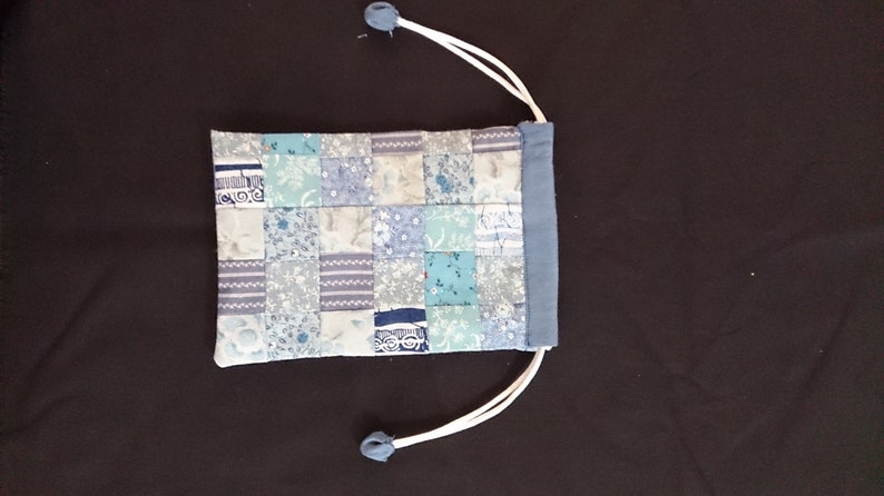 May include: A small blue drawstring bag with a patchwork design of various shades of blue and white fabric.