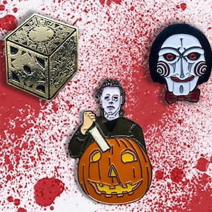May include: Three horror movie themed enamel pins. A gold cube with intricate details, a black and white pin of a character with a red and white mask, and a pin of a character holding a pumpkin.