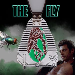 May include: A silver metal pin with a green and brown image of a creature inside a teleportation pod. The text "THE FLY" is above the pod.