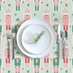 May include: A green and pink patterned tablecloth with a white plate and silverware. The tablecloth features a repeating pattern of nutcracker soldiers.
