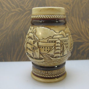 May include: A ceramic beer stein with a brown and white design featuring a ship and a city skyline. The stein has a rope-like design around the top and the words "Continent & Brigantine" on the bottom.