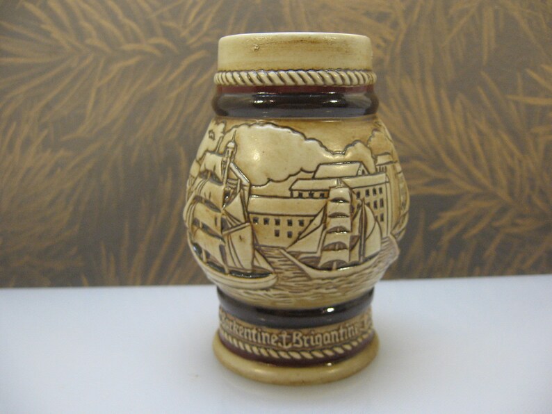 May include: A ceramic beer stein with a brown and white design featuring a ship and a city skyline. The stein has a rope-like design around the top and the words "Continent & Brigantine" on the bottom.