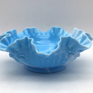 May include: A light blue glass bowl with a ruffled edge and a floral design. The bowl is made of milk glass and has a vintage look.