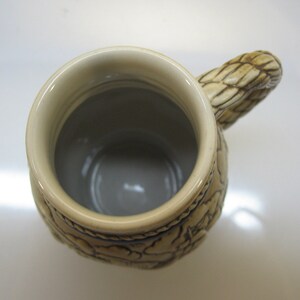 May include: A ceramic beer stein with a brown and white design. The stein has a handle shaped like a braided rope. The inside of the stein is white.