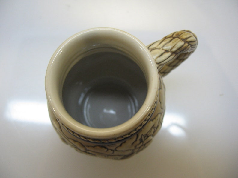 May include: A ceramic beer stein with a brown and white design. The stein has a handle shaped like a braided rope. The inside of the stein is white.