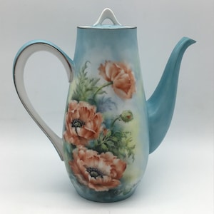 May include: A blue ceramic teapot with a white lid and handle. The teapot is decorated with a floral design of orange poppies.