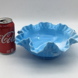 May include: A light blue glass bowl with a ruffled edge. The bowl is about the size of a standard can of soda.