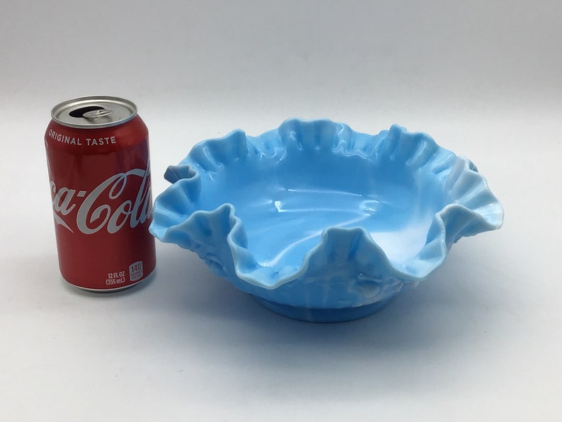 May include: A light blue glass bowl with a ruffled edge. The bowl is about the size of a standard can of soda.