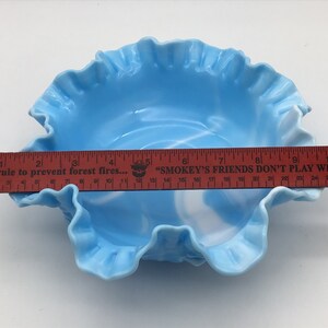 May include: A light blue glass bowl with a ruffled edge and a white swirl design. The bowl is approximately 9 inches in diameter.
