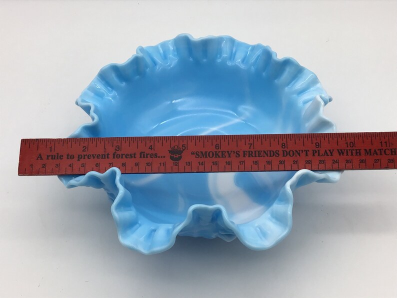 May include: A light blue glass bowl with a ruffled edge and a white swirl design. The bowl is approximately 9 inches in diameter.