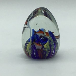 以下が含まれることがあります： 青い、緑色、オレンジ色の魚が閉じ込められたガラス製のペーパーウェイト。魚は泡のある透明な液体の中で泳いでいます。