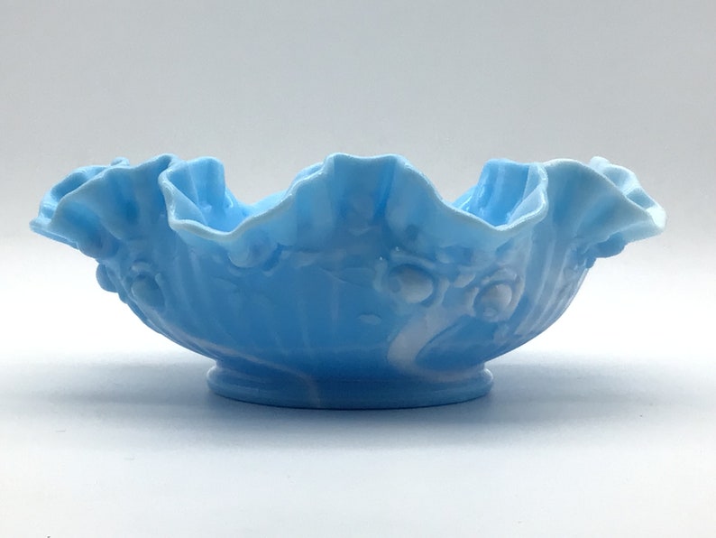 May include: A light blue glass bowl with a ruffled edge and a white floral design.