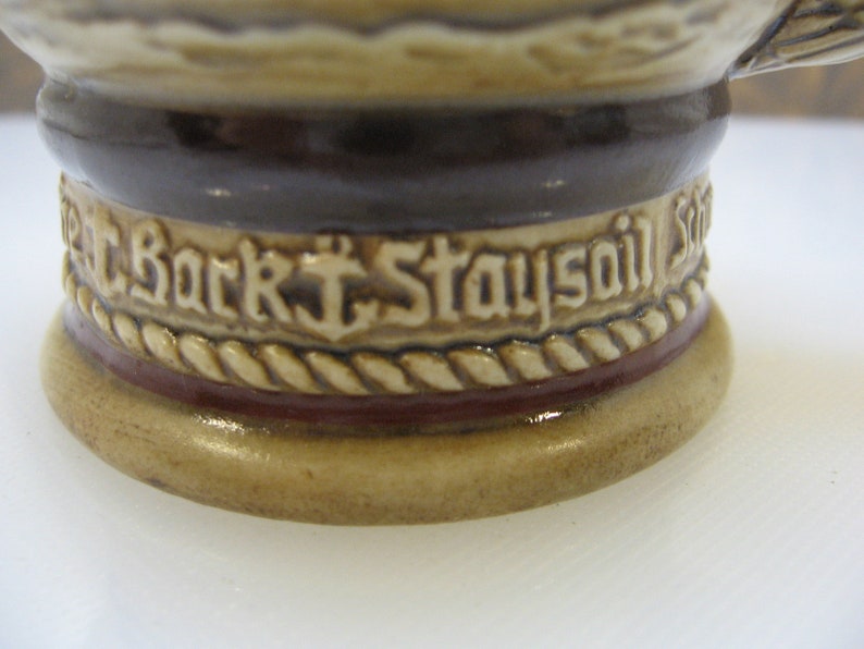 May include: Close-up of a ceramic stein with a brown and white rope design and the text "Bark Staysail" in white.