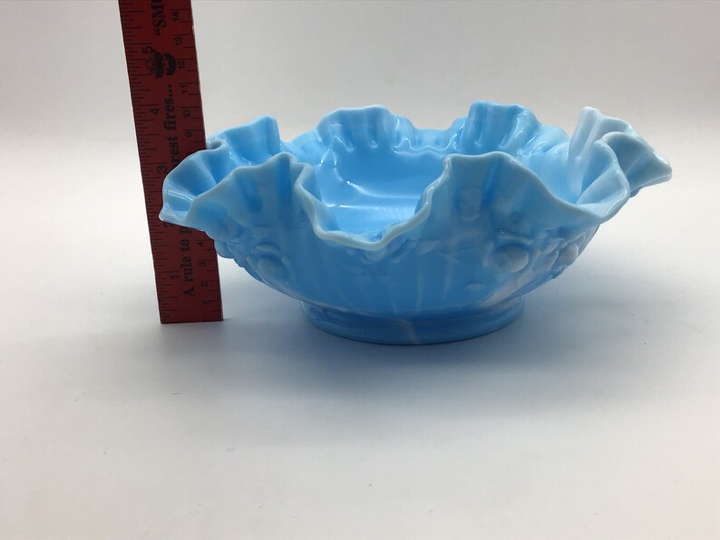 May include: A light blue glass bowl with a ruffled edge and a floral design. The bowl is approximately 5 inches in diameter.