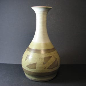 May include: A ceramic vase with a tall, slender neck and a rounded body. The vase is decorated with a geometric pattern in shades of brown and green.