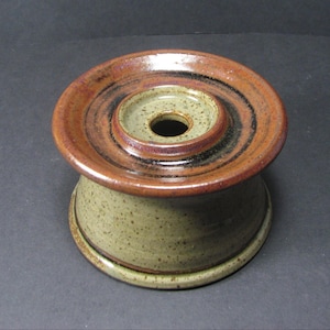 May include: A brown and green ceramic inkwell with a wide, flat top and a smaller, round opening in the centre.