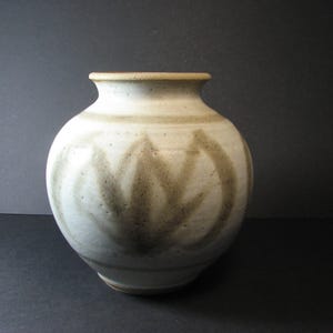 May include: A handmade ceramic vase with a rounded form and a slender neck. The vase is mainly off-white with a textured finish and displays a repeating, abstract design in brown tones. The rim and base have a darker brown accent.