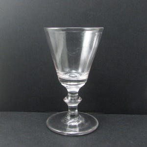 May include: A clear, stemmed glass with a wide, conical bowl and a round base. The stem has a decorative, bulbous design. The glass is empty and reflects the surroundings. Likely used for serving drinks.
