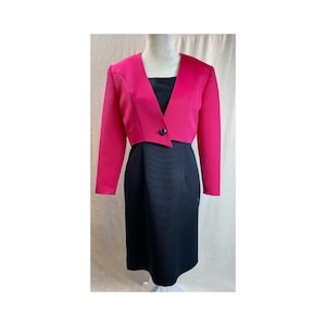 May include: A black and hot pink dress suit with a cropped jacket and a single button closure. The jacket has a pointed collar and long sleeves.