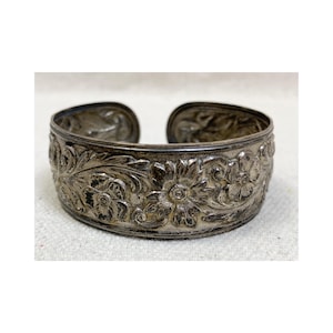 May include: A silver cuff bracelet with an intricate floral design. The bracelet is made of metal and has a smooth, polished finish.