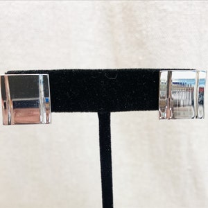 May include: A pair of silver earrings with a rectangular shape and a smooth, reflective surface.