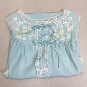 May include: A light blue sleeveless nightgown with white lace trim and floral embroidery. The gown has a V-neckline and ties at the neckline.
