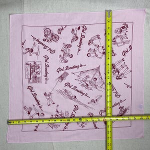 May include: A light pink square bandana with a maroon border and illustrations of Girl Scout activities. The text "Girl Scouting is..." is repeated around the edges. The bandana measures approximately 22 inches by 22 inches.