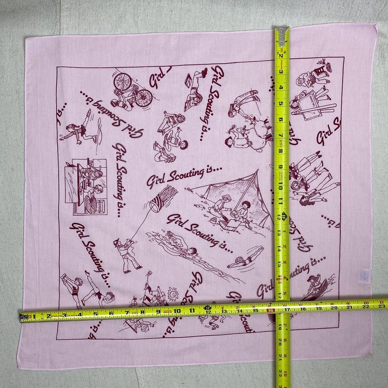 May include: A light pink square bandana with a maroon border and illustrations of Girl Scout activities. The text "Girl Scouting is..." is repeated around the edges. The bandana measures approximately 22 inches by 22 inches.