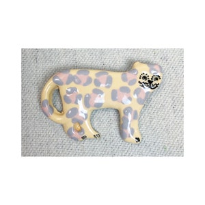 May include: A ceramic figurine of a leopard with a light yellow base and pink and purple spots. The figurine has black eyes and a black nose.