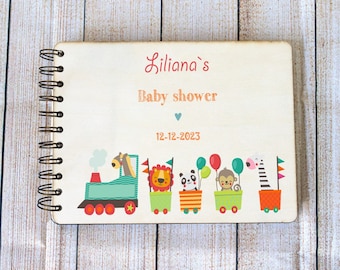 May include: A wooden baby shower guest book with a spiral binding. The cover features a colorful illustration of a train with animals, including a lion, panda, monkey, and zebra. The text on the cover reads "Liliana's Baby Shower 12-12-2023".