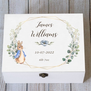 May include: White wooden keepsake box with a watercolor illustration of Peter Rabbit and floral wreath. The box is personalized with the name "James Williams", date "10-07-2022", and weight "6lb 7oz". A gold geometric frame surrounds the text.