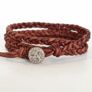 Peut inclure: Un bracelet en cuir marron avec une fermeture bouton argentée. Le bouton a un motif floral blanc.