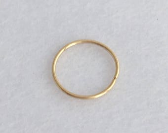 May include: A small, thin, gold-colored nose ring. The ring is a simple, seamless circle, likely made of metal. The jewelry is set against a white background.