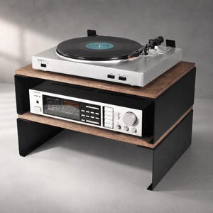 Op de afbeelding: Een audio-meubel met twee niveaus, voorzien van donkerhouten planken en zwarte metalen zijpanelen. Op de bovenste plank staat een zilverkleurige platenspeler met een zwarte vinylplaat, en op de onderste plank een zilverkleurige stereo-ontvanger.