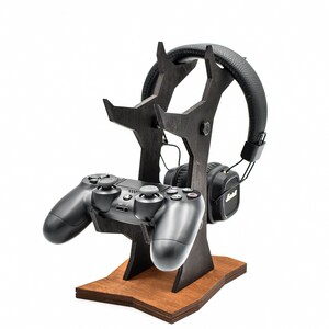 May include: A black wooden stand with a star-shaped base holds a black video game controller and black headphones. The stand is designed to hold the headphones and controller upright.
