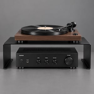 Op de afbeelding: Een zwart metalen plank draagt een houten platenspeler met een zwarte draaischijf en toonarm. Onder de plank staat een zwarte Denon audioversterker met aan-uitknop, hoofdtelefoonaansluiting, bas-, treble-, balansregelaars en een grote volumeknop.