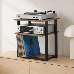 May include: A three-tier media storage stand with a black metal frame and brown wood-grain shelves. The top shelf holds a silver turntable, the middle shelf holds a silver audio receiver, and the bottom shelf contains a collection of vinyl records.