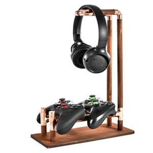 Op de afbeelding: Een houten standaard met koperen buizen houdt een zwarte koptelefoon en twee zwarte videogamecontrollers.