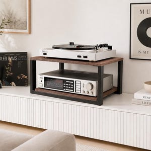 May include: A two-tier audio component stand featuring a dark wood grain finish on the shelves and a sturdy black metal frame. The stand holds a silver turntable on the top shelf and a silver stereo receiver with multiple buttons on the bottom shelf.