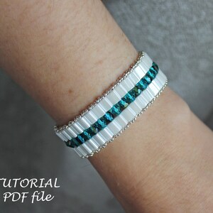 May include: A white and teal beaded bracelet with a silver accent. The bracelet is on a person's wrist.  TUTORIAL PDF file