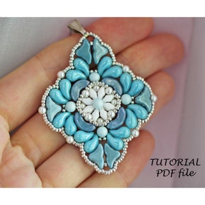 Könnte beinhalten: Ein blauer und weißer Perlenanhänger mit einer silbernen Öse. Der Anhänger hat die Form eines Quadrats mit abgerundeten Ecken und zeigt ein Blumenmuster. Der Anhänger wird in einer Hand gehalten. Der Text "TUTORIAL PDF file" ist in der unteren rechten Ecke des Bildes sichtbar.