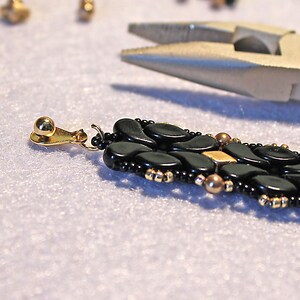 Peut inclure: Gros plan sur une boucle d'oreille noire et dor&eacute;e avec un fermoir crochet dor&eacute;. La boucle d'oreille est faite de petites perles noires et dor&eacute;es, et le crochet est en m&eacute;tal dor&eacute;.