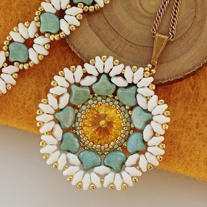 May include: A white and gold beaded necklace with a green and gold pendant. The pendant is a circular design with a yellow crystal in the center.