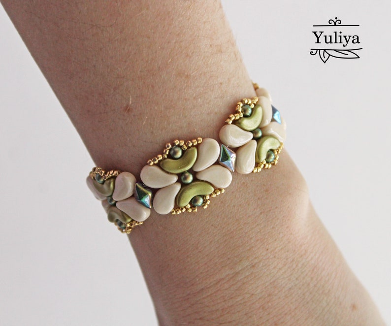 Op de afbeelding: Een witte en groene kralen armband met gouden accenten. De armband is gemaakt van kleine, ronde kralen en heeft een bloemmotief.