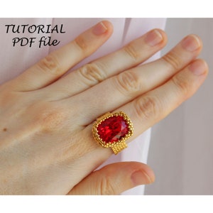 Puede incluir: Un anillo de oro con una gran piedra preciosa roja facetada. El anillo está en una mano.