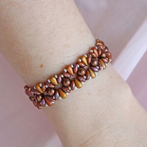 Peut inclure: Un bracelet en perles brunes et dor&eacute;es avec des perles blanches tiss&eacute;es. Le bracelet est port&eacute; au poignet.