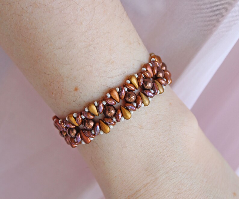 Peut inclure: Un bracelet en perles brunes et dor&eacute;es avec des perles blanches tiss&eacute;es. Le bracelet est port&eacute; au poignet.